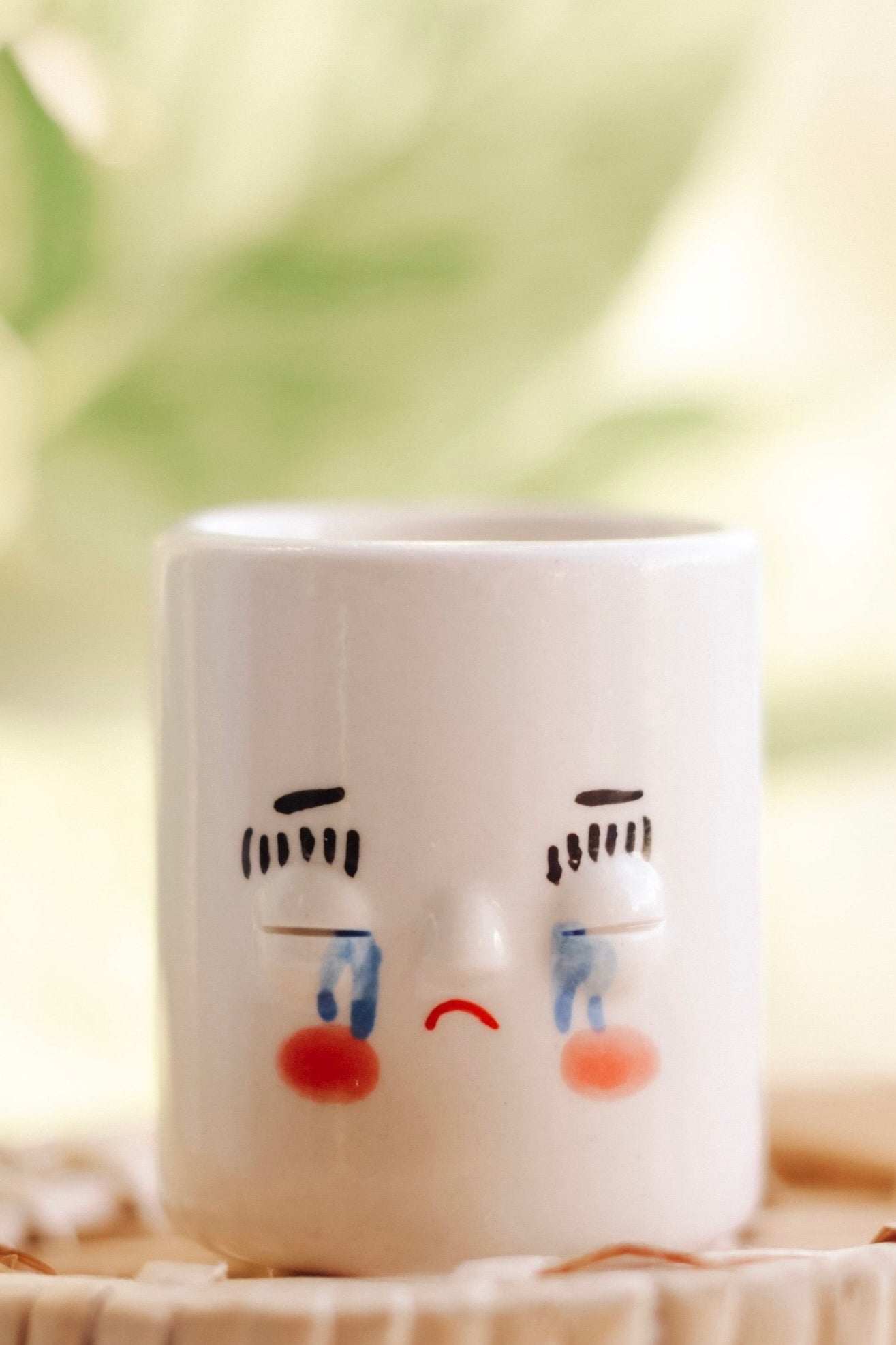 Small white glossy pot with a painted crying face and rosy cheeks. 