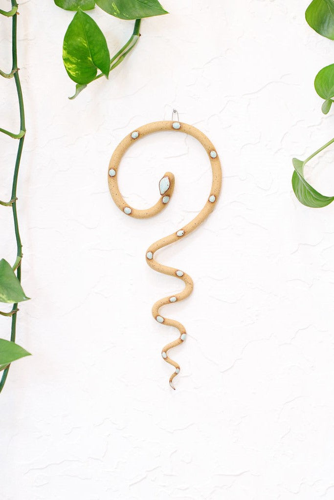 Simple contemporary ceramic snake wall decoration, with the top of the snake shaped loosely like a question mark and the tail hangs down in an organic s curve. This snake is Selma, speckled tan clay with light turquoise glazed head and dots.