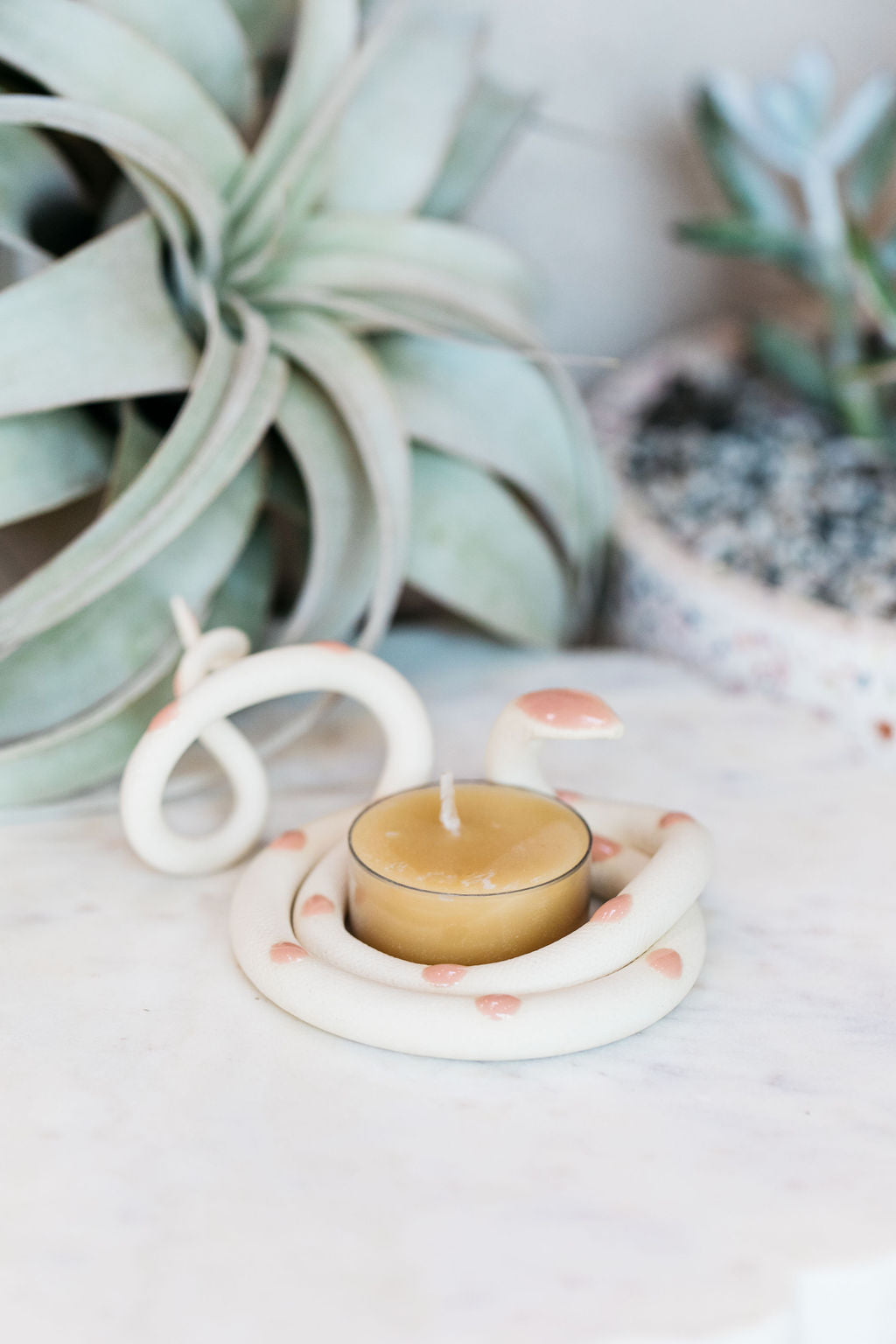 Organically coiled ivory clay snake with pastel pink head and dots. This colorway is Sofie. Styled with a beeswax tea light that sits in the center of the coil.