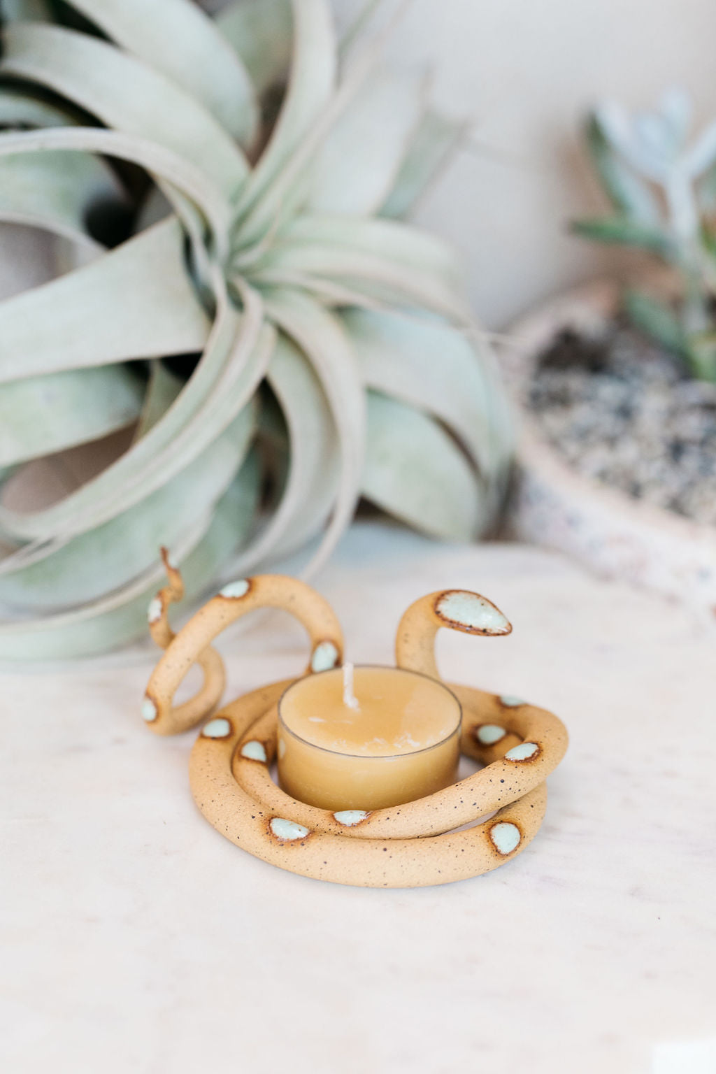 Organically coiled speckled tan clay snake with turquoise head and dots. This colorway is Selma. Styled with a beeswax tea light that sits in the center of the coil.