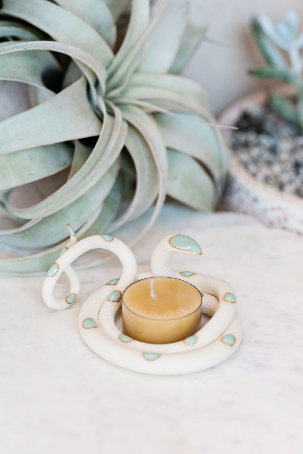 Organically coiled ivory clay snake with turquoise head and dots. This colorway is Sylvia. Styled with a beeswax tea light that sits in the center of the coil.
