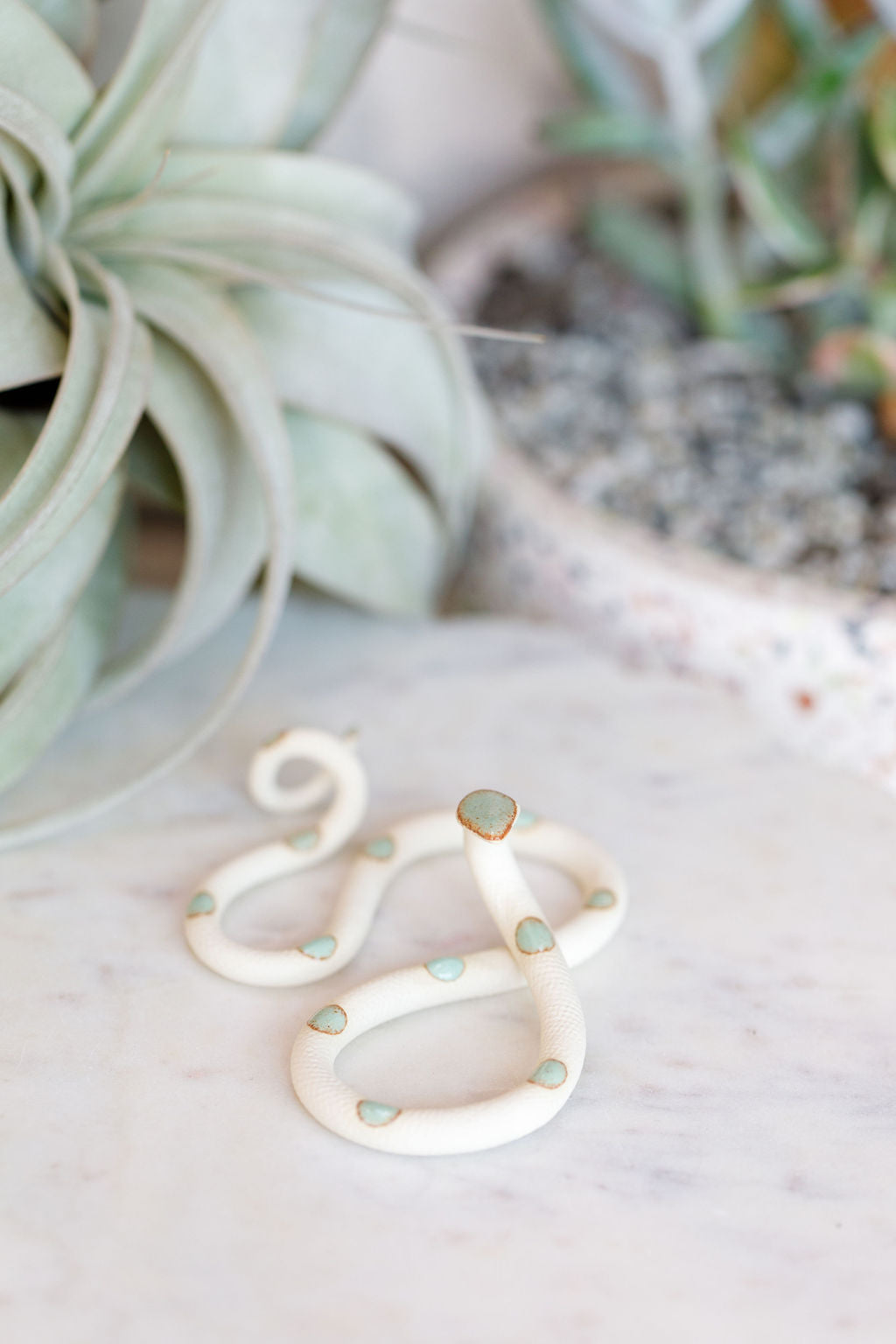 Small organic s-shaped pottery snake sculpture in the colorway Sylvia, ivory white clay body with a light turquoise glazed head and evenly spaced glazed dots.