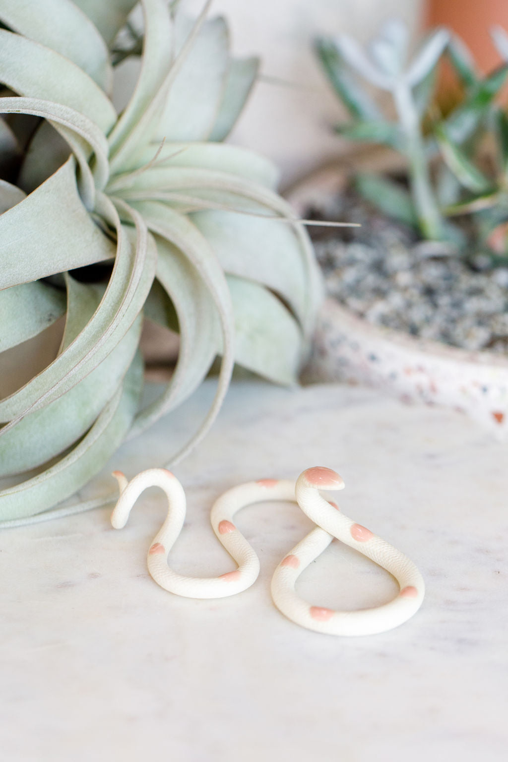  Small organic s-shaped pottery snake sculpture  in the colorway Sofie, ivory white clay body with a light pink glazed head and evenly spaced glazed dots along its body.