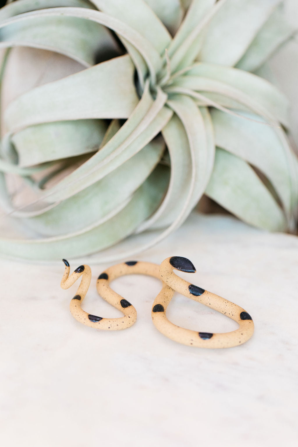 Small organic s-shaped pottery snake sculpture in the colorway Sammy, a speckled tan clay body with a black glazed head and evenly spaced small dots.