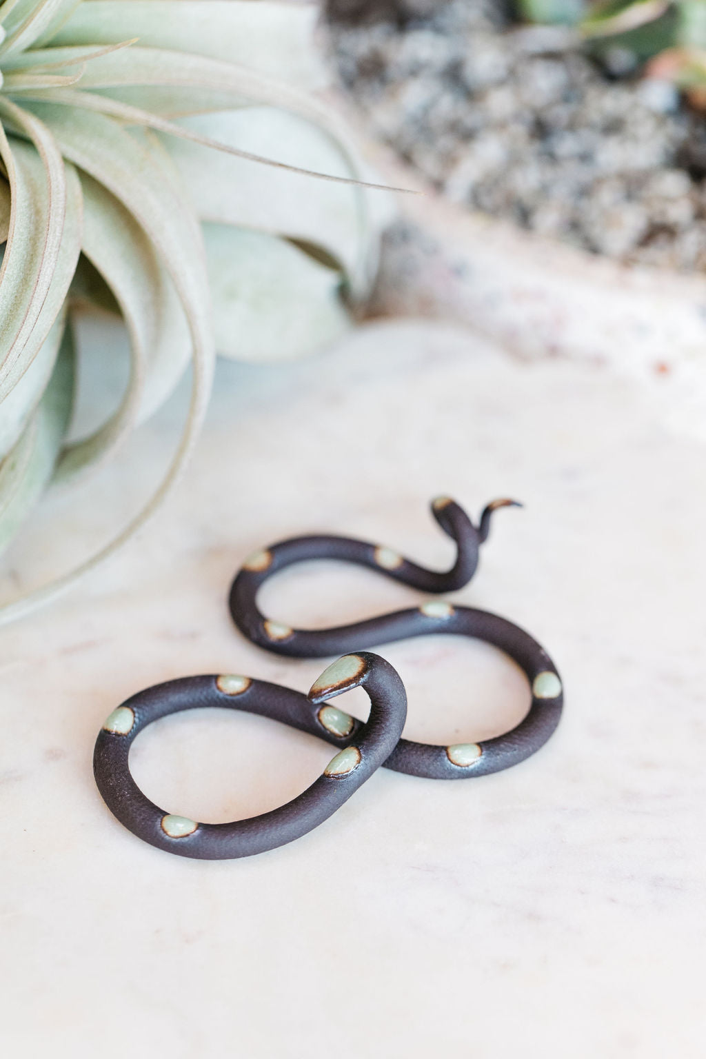 Small organic s-shaped pottery snake sculpture in the colorway Stevie, a matte black clay body with a light turquoise glazed head and evenly spaced glazed dots.