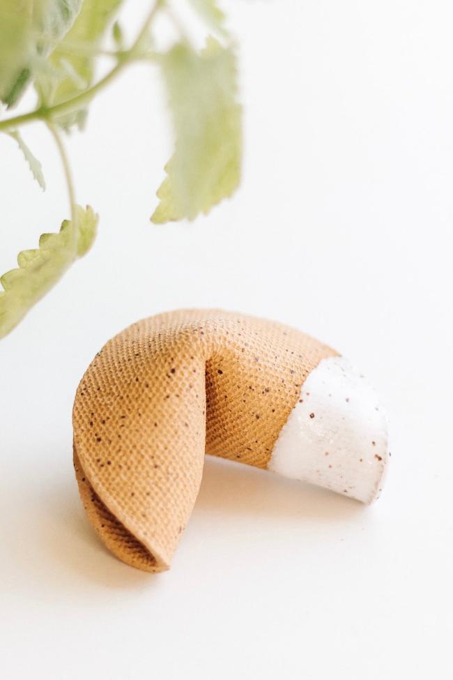 Ceramic speckled tan fortune cookie with one side dipped in an opaque white glaze