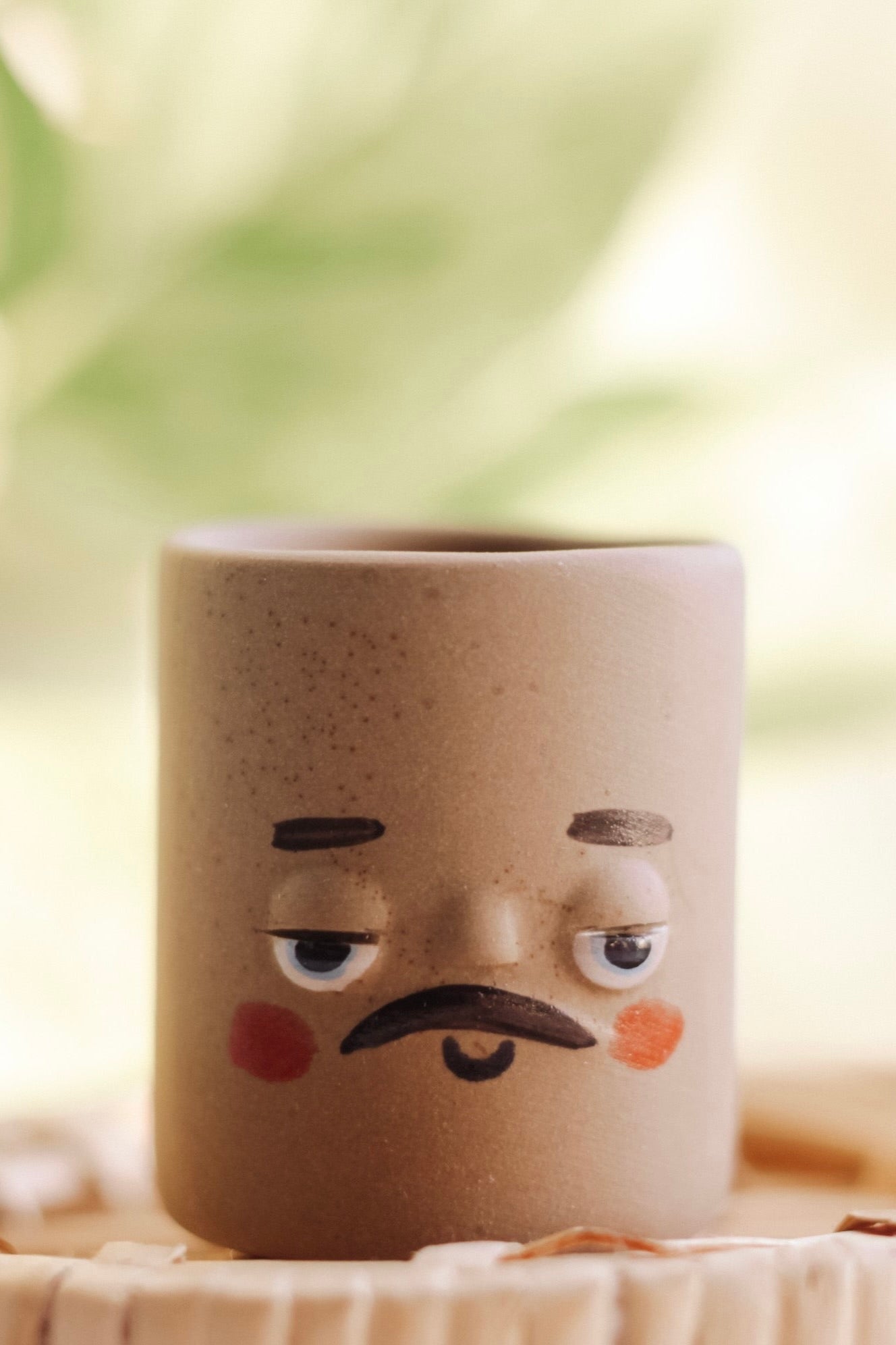 Small brown pot with a painted face featuring a mustache and rosy cheeks. 