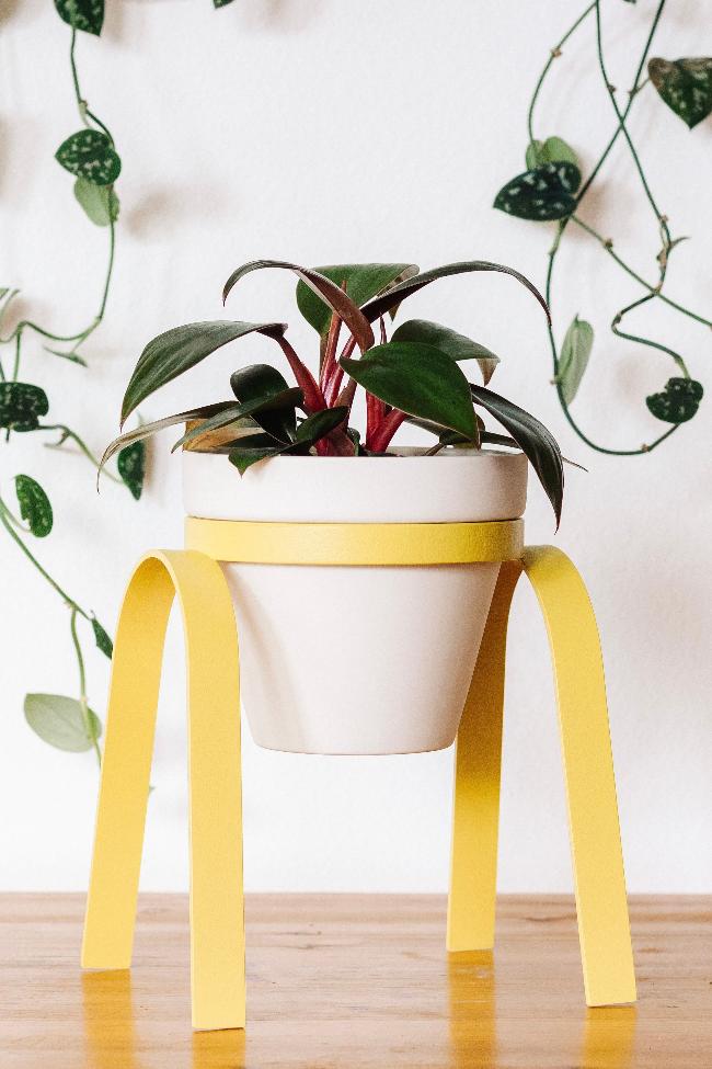 Bright yellow lifted metal plant stand holding a white porcelain pot with a planted houseplant