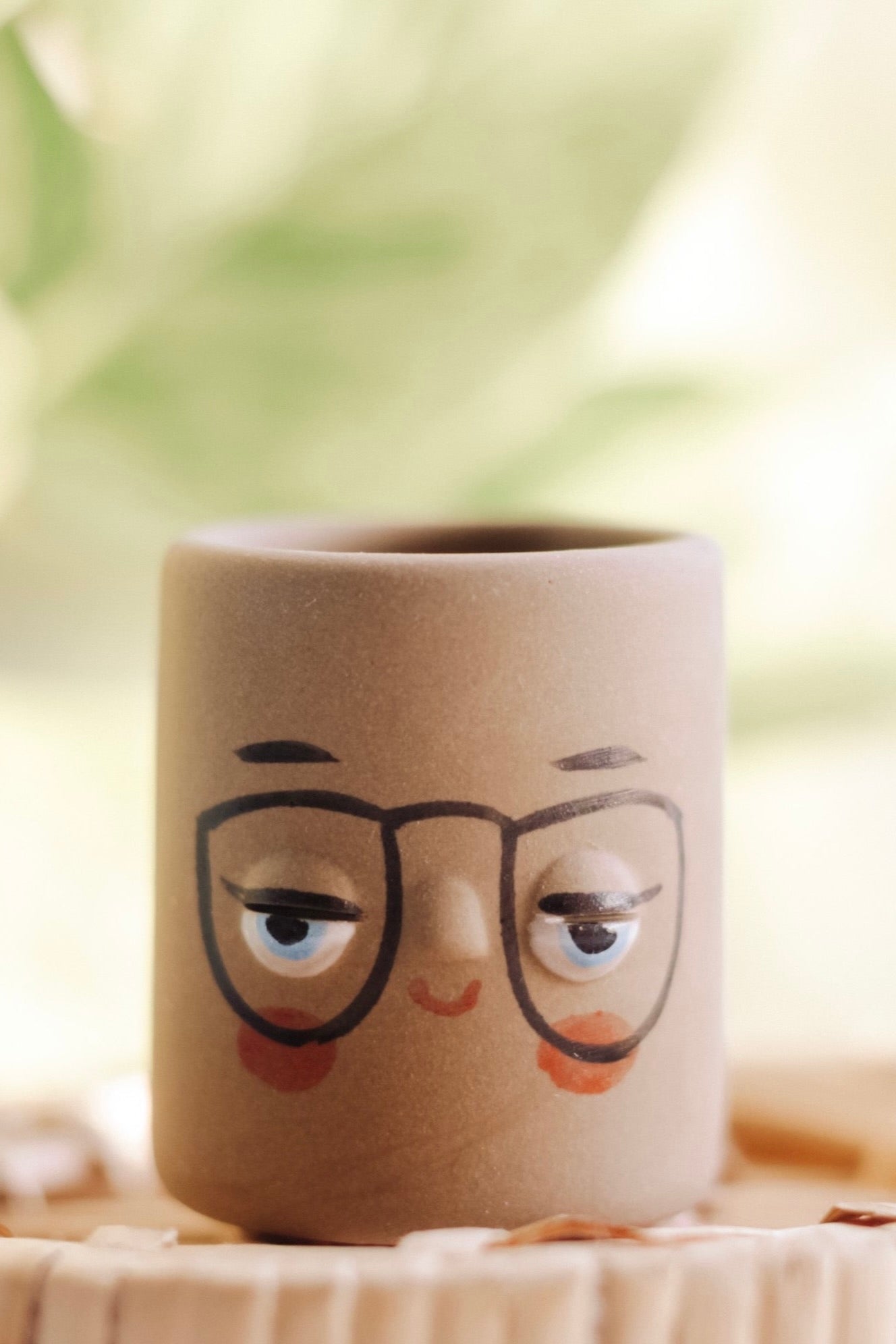 Small brown pot with a painted face featuring glasses and rosy cheeks. 