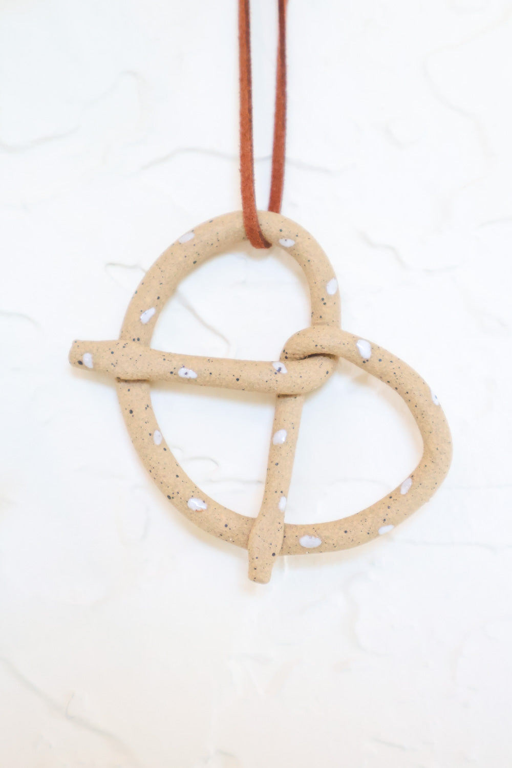Close up for the tan clay pretzel shaped ornament. White glaze dots mimic salt sprinkles. 