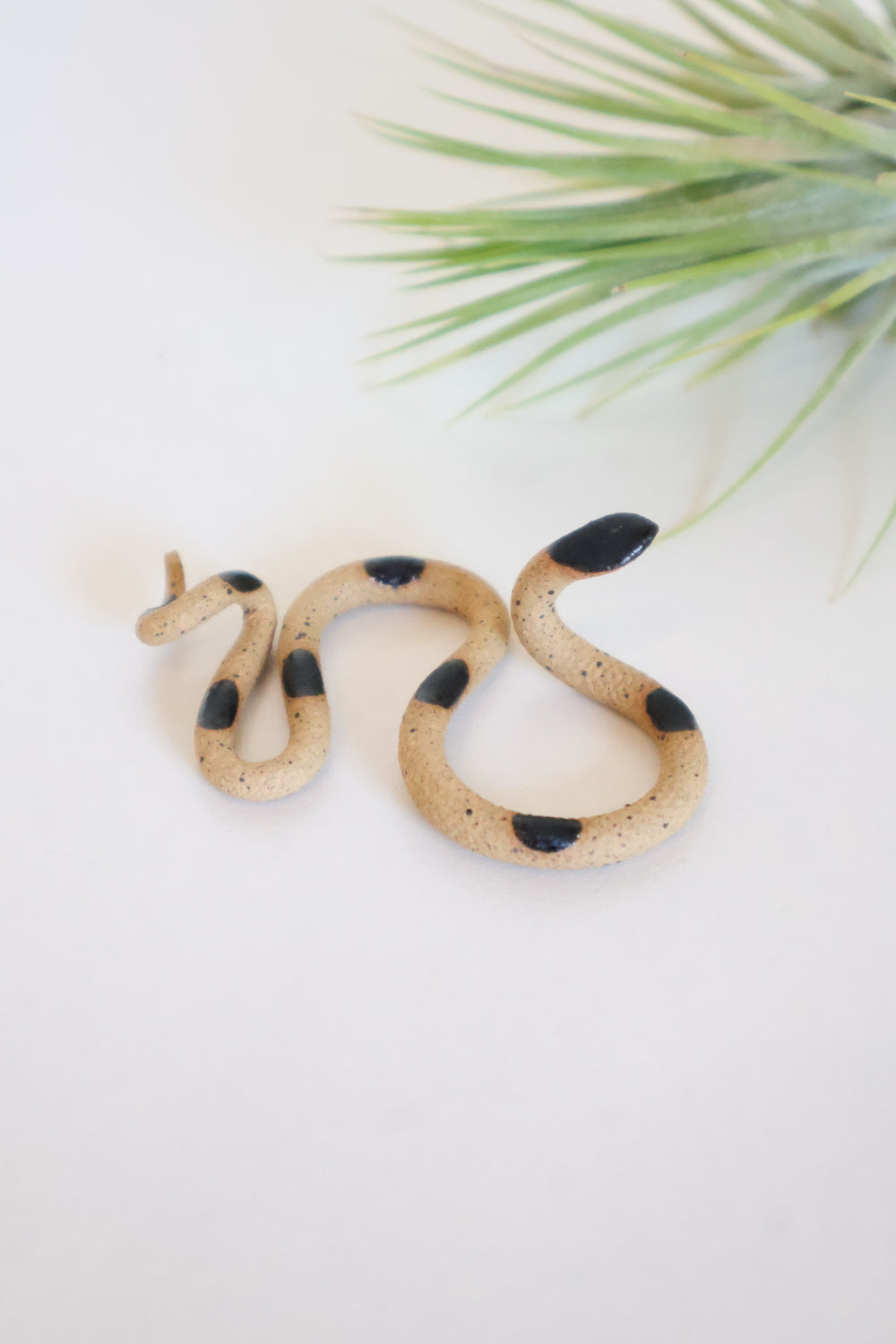 Itty bitty organic s-shaped pottery snake sculpture in the colorway Sammy, speckled brown clay body with a black glazed head and evenly spaced glazed dots along its body.