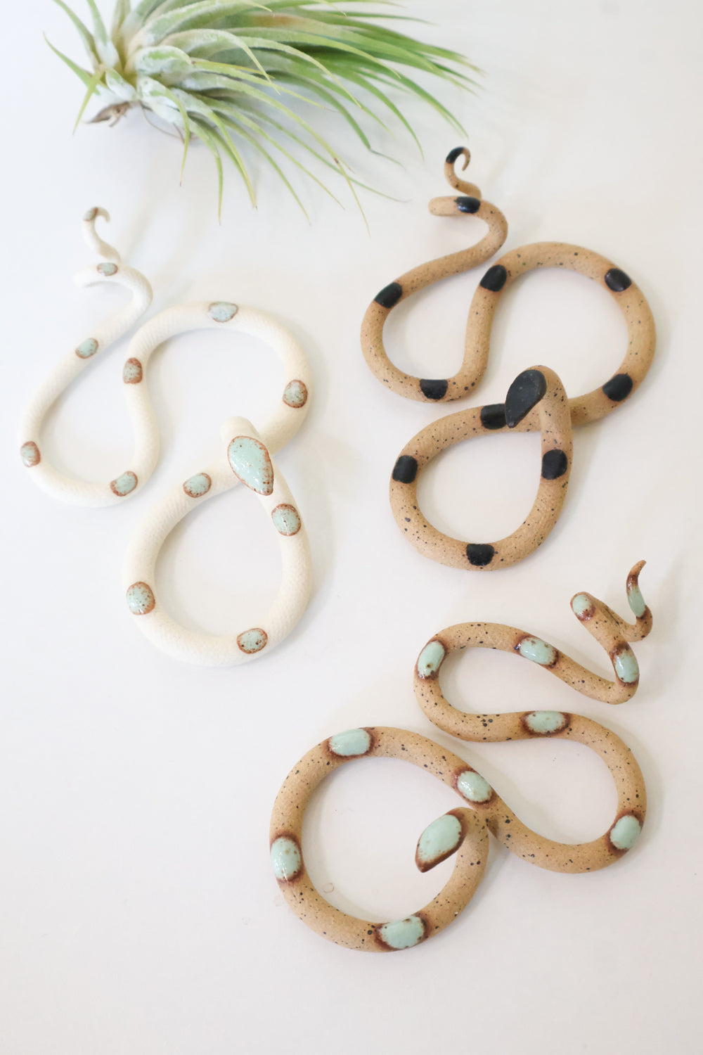 Desert curated set of three small ceramic snakes in the following colorways, Sylvia (ivory clay with light turquoise glaze dots), Selma (speckled tan clay with light turquoise glaze dots), and Sammy (speckled tan with black glaze dots).
