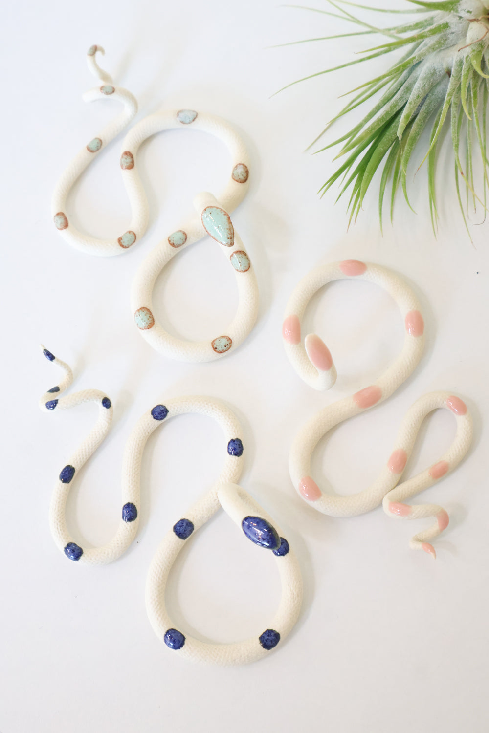 Garden curated set of three small ceramic snakes in the following colorways, Sylvia (ivory clay with light turquoise glaze dots), Sofie (ivory clay with light pink glaze dots), and Selena (ivory clay with royal blue glaze dots).