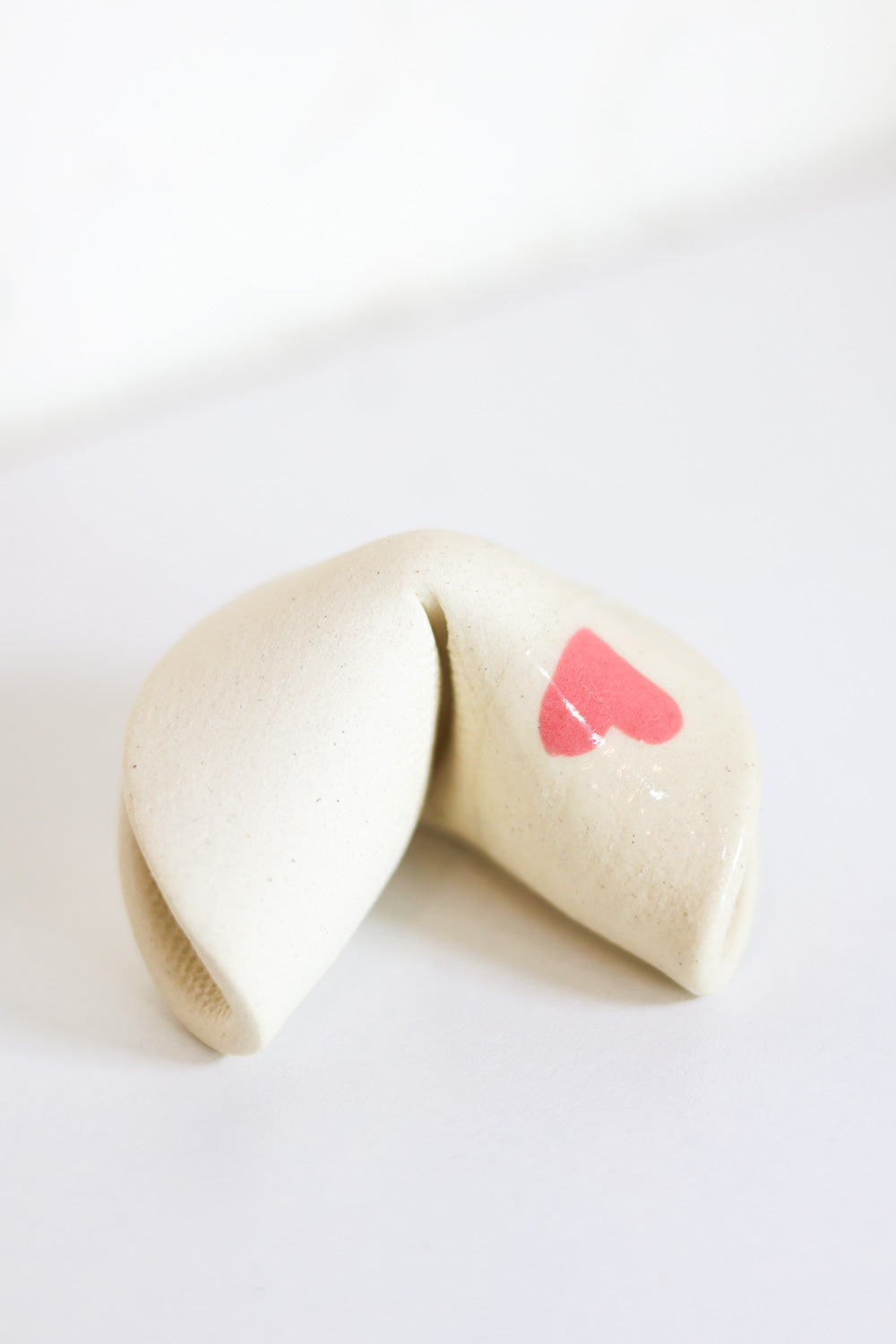 Ceramic fortune cookie made from ivory clay with a little pink heart on one side