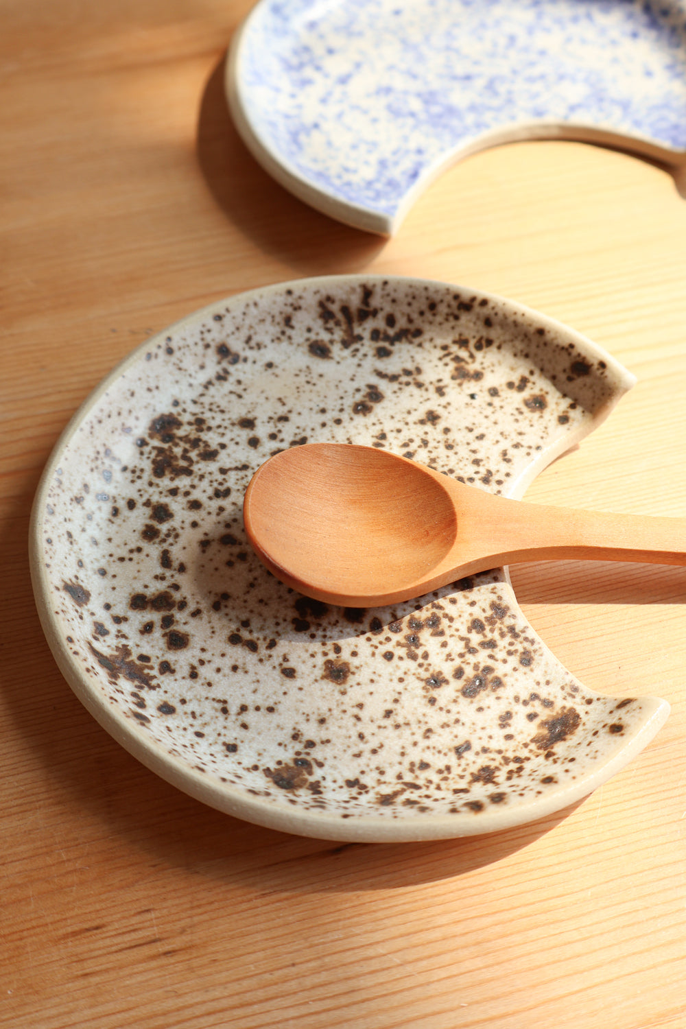 Speckled brown and tan ceramic plate displayed with a wooden spoon on a wooden surface