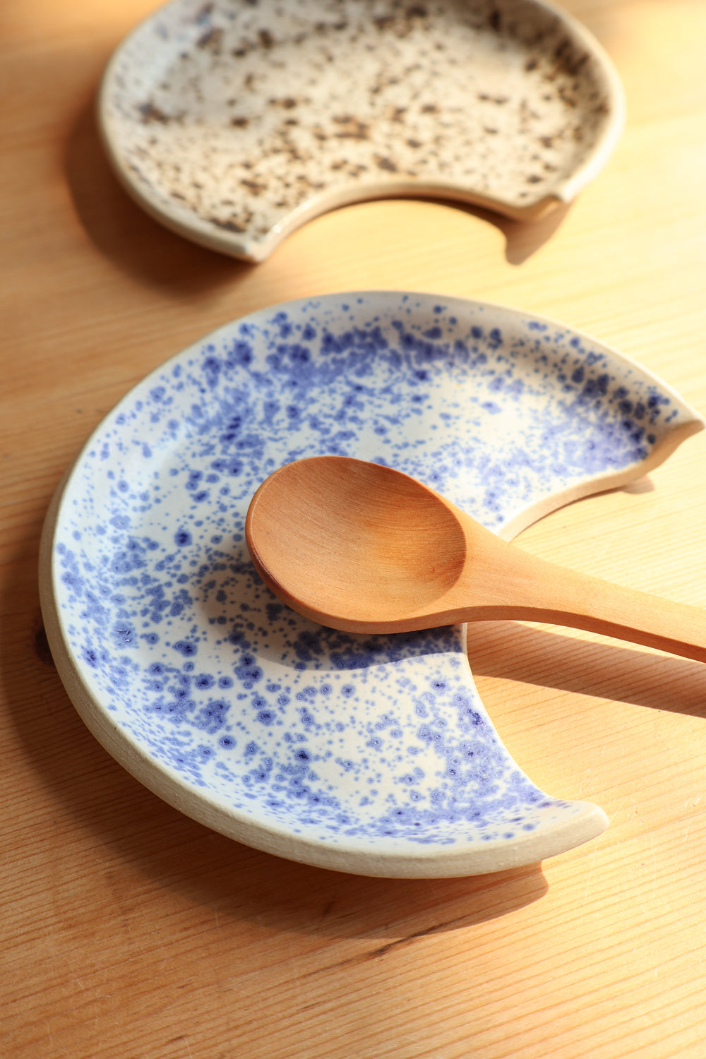 Speckled ceramic plate with blue patterns on a wooden surface, accompanied by a wooden spoon.