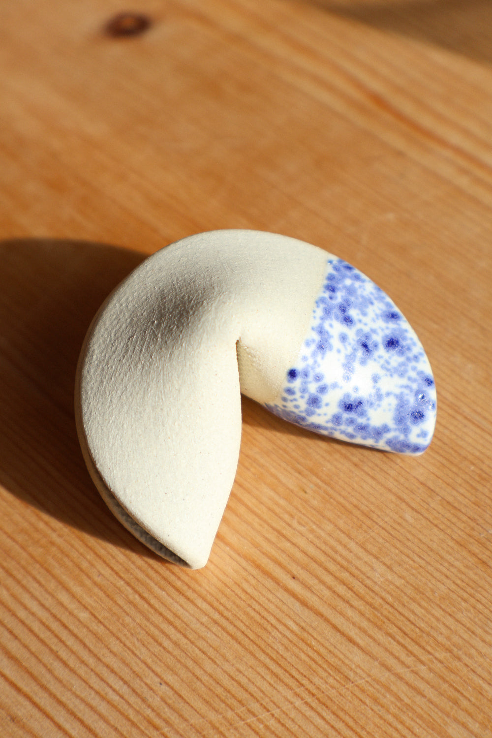 Ivory clay fortune cookie sculpture with one side dipped in a speckled blue glaze