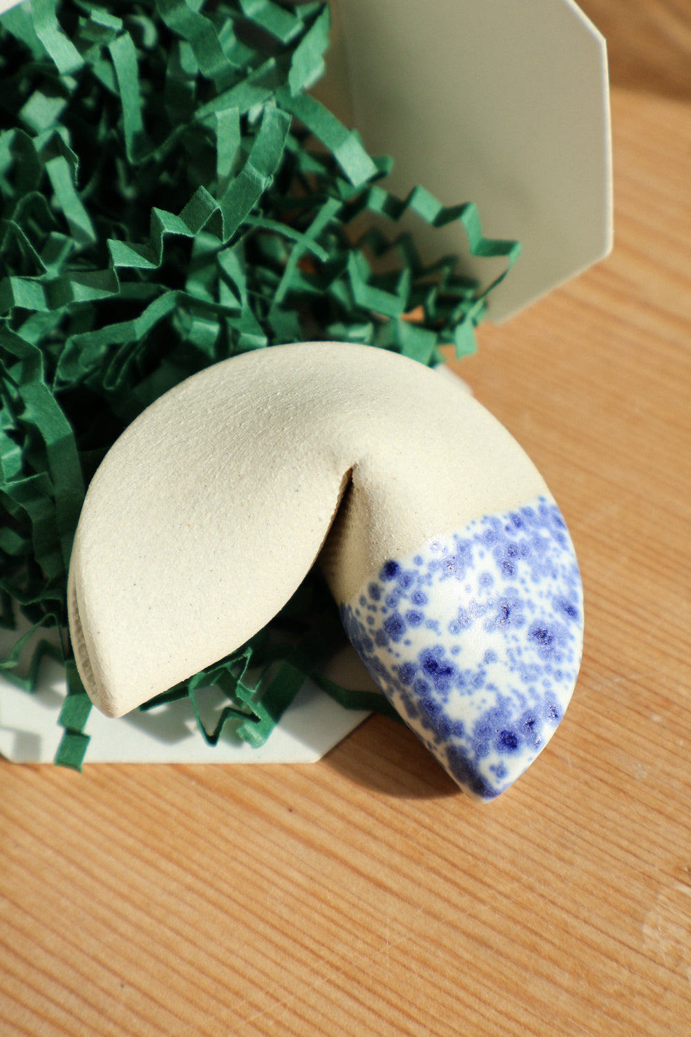 Handmade clay fortune cookie with blue and white dipped design a wooden surface