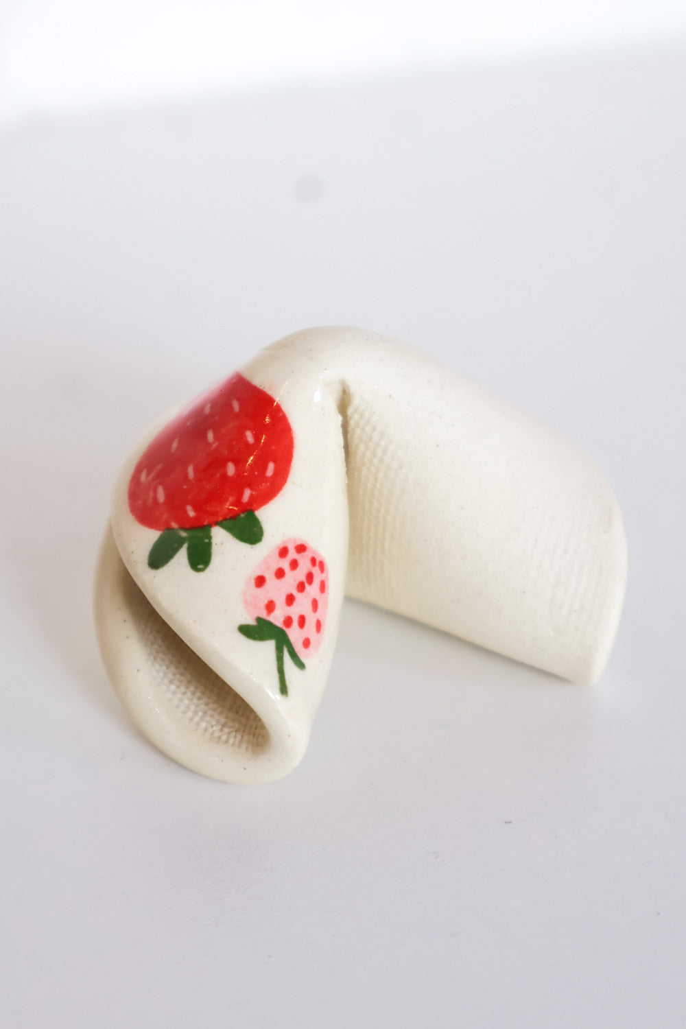 Ceramic fortune cookie made from ivory clay with a red and pink strawberry decal on one corner.