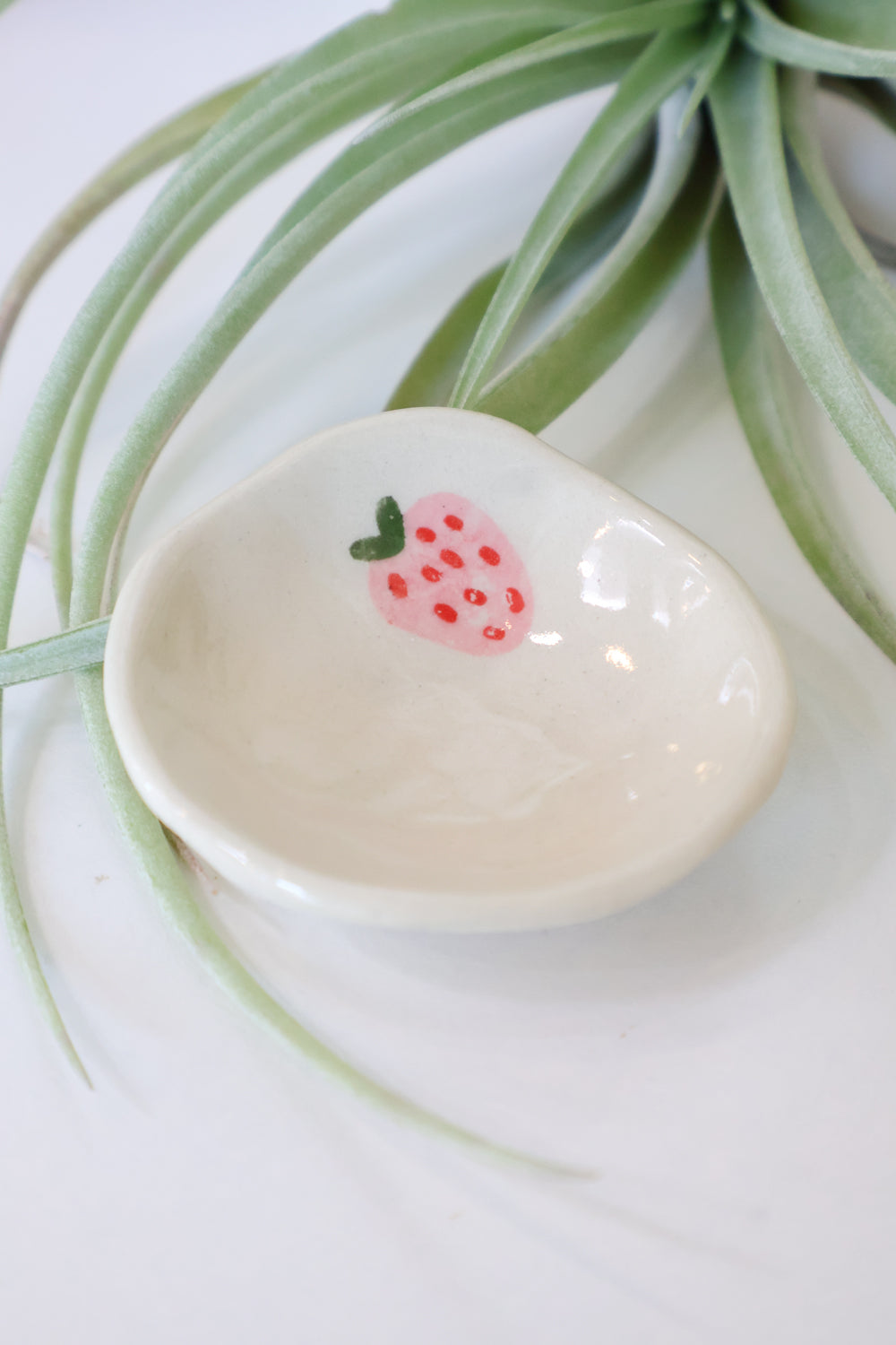 Small white ceramic dish with a pink strawberry decal on a light background